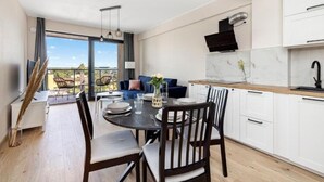 A modern kitchen with white cabinets, a dining area with a round table, and a view of the outdoors. - Holiday Apartment Right Next to the Beach Darlowko (Darlowo)