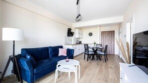 A modern living room with a blue sofa, a white coffee table, and a dining area with a table and chairs. - Holiday Apartment Right Next to the Beach Darlowko (Darlowo)