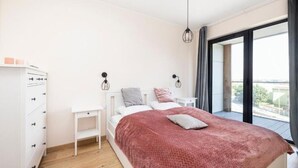 A bedroom with a bed, bedside tables, a wardrobe, and a view through a large window. - Holiday Apartment Right Next to the Beach Darlowko (Darlowo)