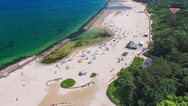 An aerial view of a beach with umbrellas, a sandy shore, and wind turbines in the distance. - Holiday Apartment Right Next to the Beach Darlowko (Darlowo)
