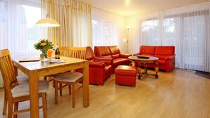 A spacious living room with a wooden dining table, red leather sofas, and a round coffee table.