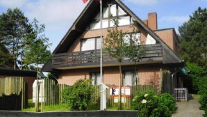 A two-story building with a pitched roof, a flagpole with a flag, and a wooden fence.
