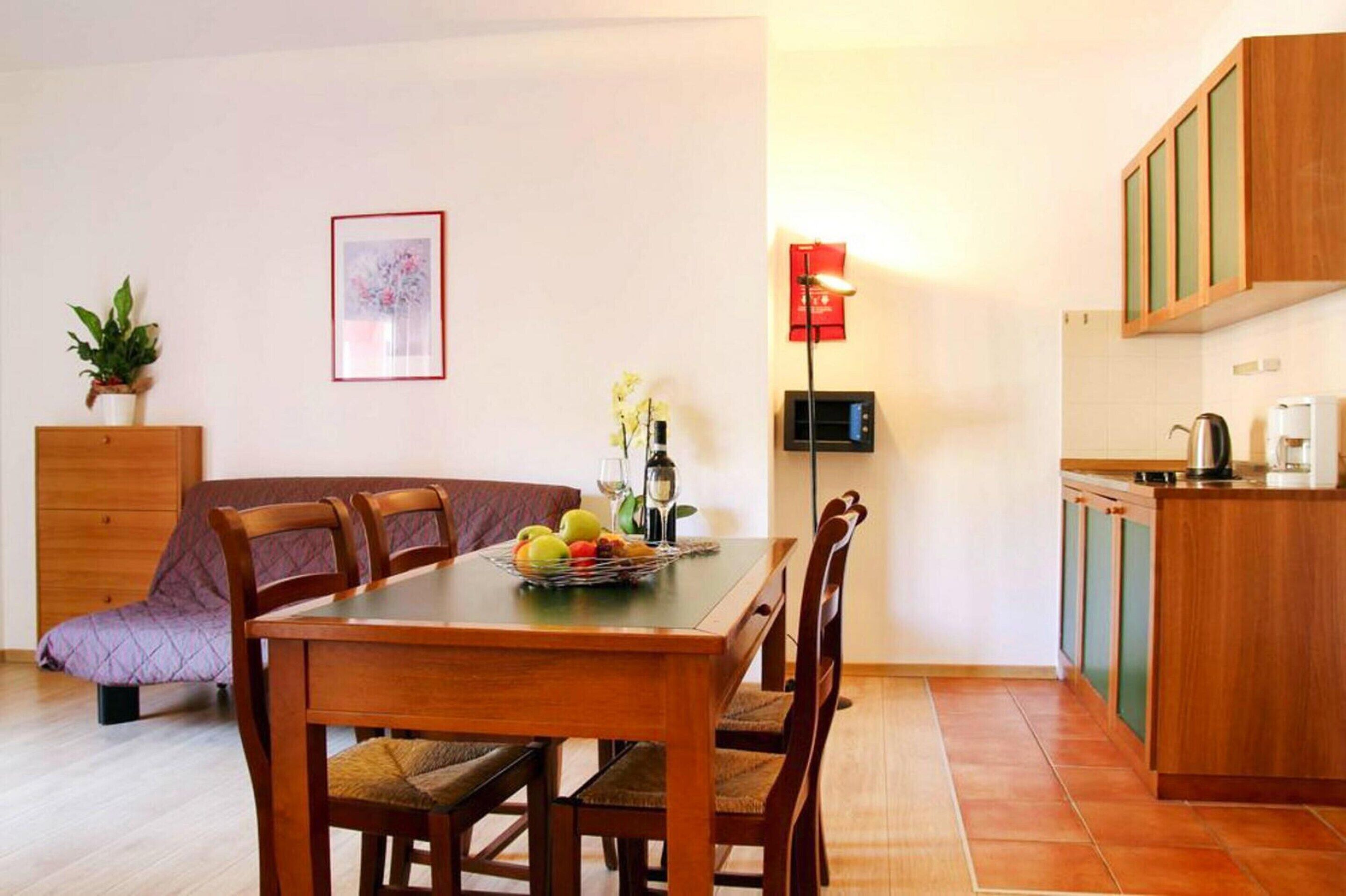 Un coin repas avec une table et des chaises en bois, un canapé, une petite plante en pot, un tableau encadré, et un espace cuisine avec des placards et un four à micro-ondes.