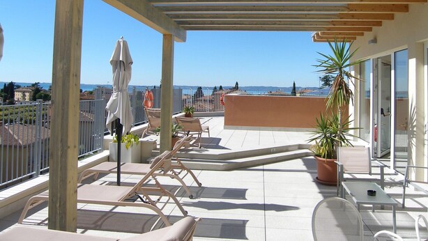 A covered outdoor area with lounge chairs, a table, and potted plants. - Apartment in Garda Near Shopping (Garda)