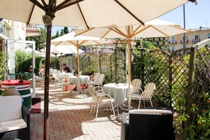 An outdoor patio with white wicker furniture, umbrellas, and a brick floor. - Apartment in Garda Near Shopping (Garda)