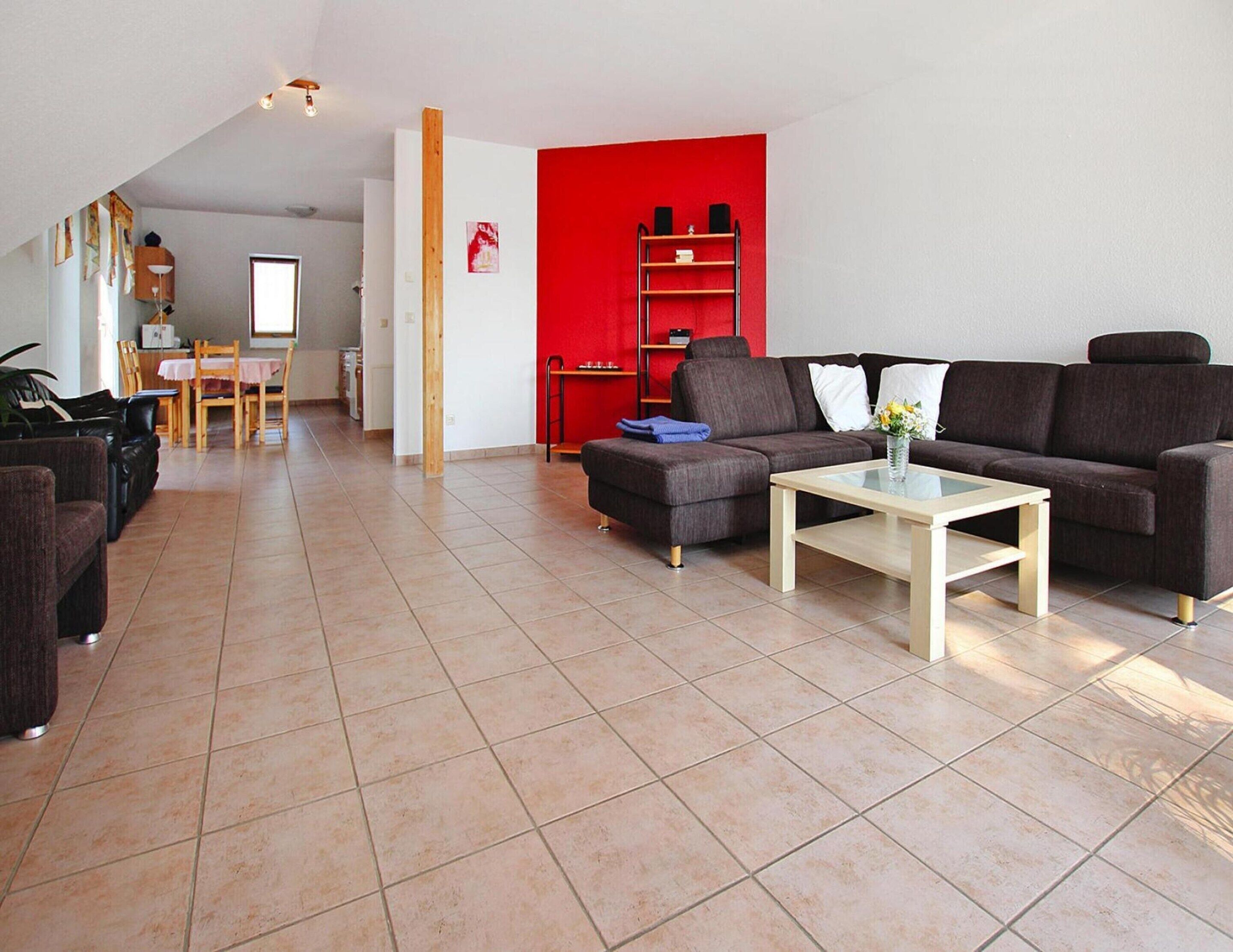 A modern living room with a brown sofa, a glass coffee table, and a red accent wall.