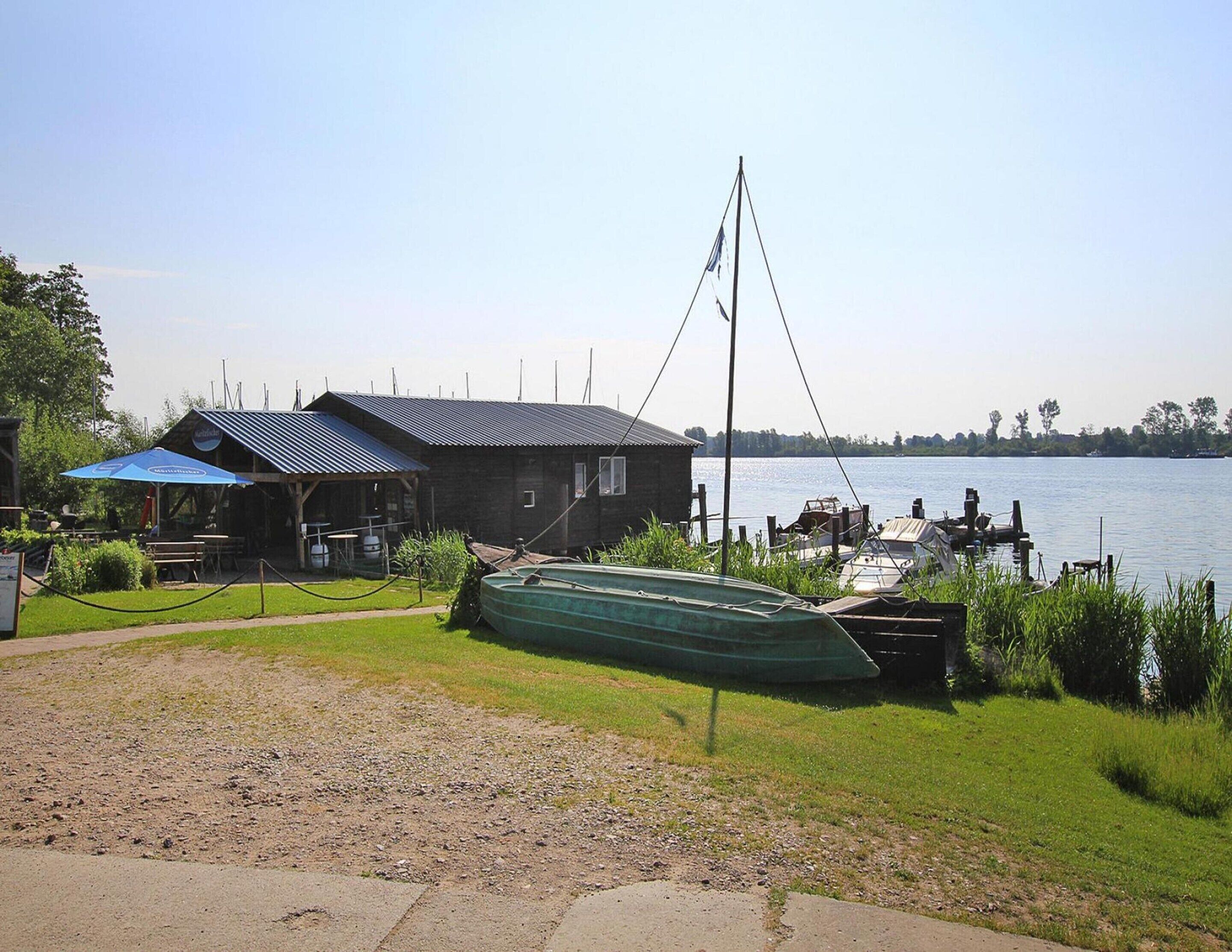 Un muelle rústico con un bote verde, un pequeño edificio de madera con techo azul y una vista despejada del agua.