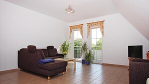 Ein Wohnzimmer mit braunem Sofa, einem Couchtisch, einem TV-Schrank und einem Balkon mit Blumentöpfen.