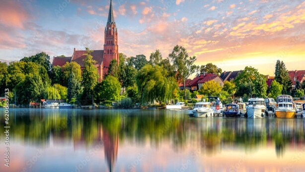 Eine friedliche Stadt am Seeufer, mit einem markanten Kirchturm, Booten, die am Ufer liegen, und üppigem Grün.