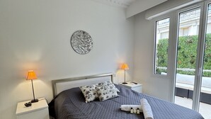 Un dormitorio con una cama grande, dos mesitas de noche, un reloj de pared y una ventana con vistas a vegetación.
