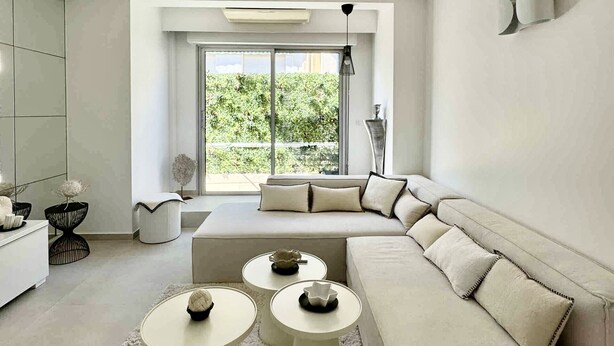 Una sala de estar moderna con un sofá modular, mesas de centro redondas y un ventanal con vistas a zonas verdes.