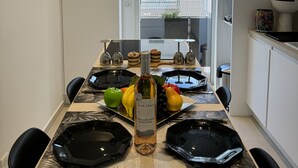 Cocina moderna con una mesa de comedor preparada para seis personas, con platos negros, una botella de vino y diversas frutas.