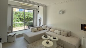Una sala de estar moderna con un sofá seccional, dos mesas redondas de centro, un amplio ventanal corredero que da a un balcón y una alfombra blanca.