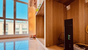 Una habitació moderna amb un finestral gran, panells de fusta i un dispositiu electrònic negre sobre una estant de fusta.