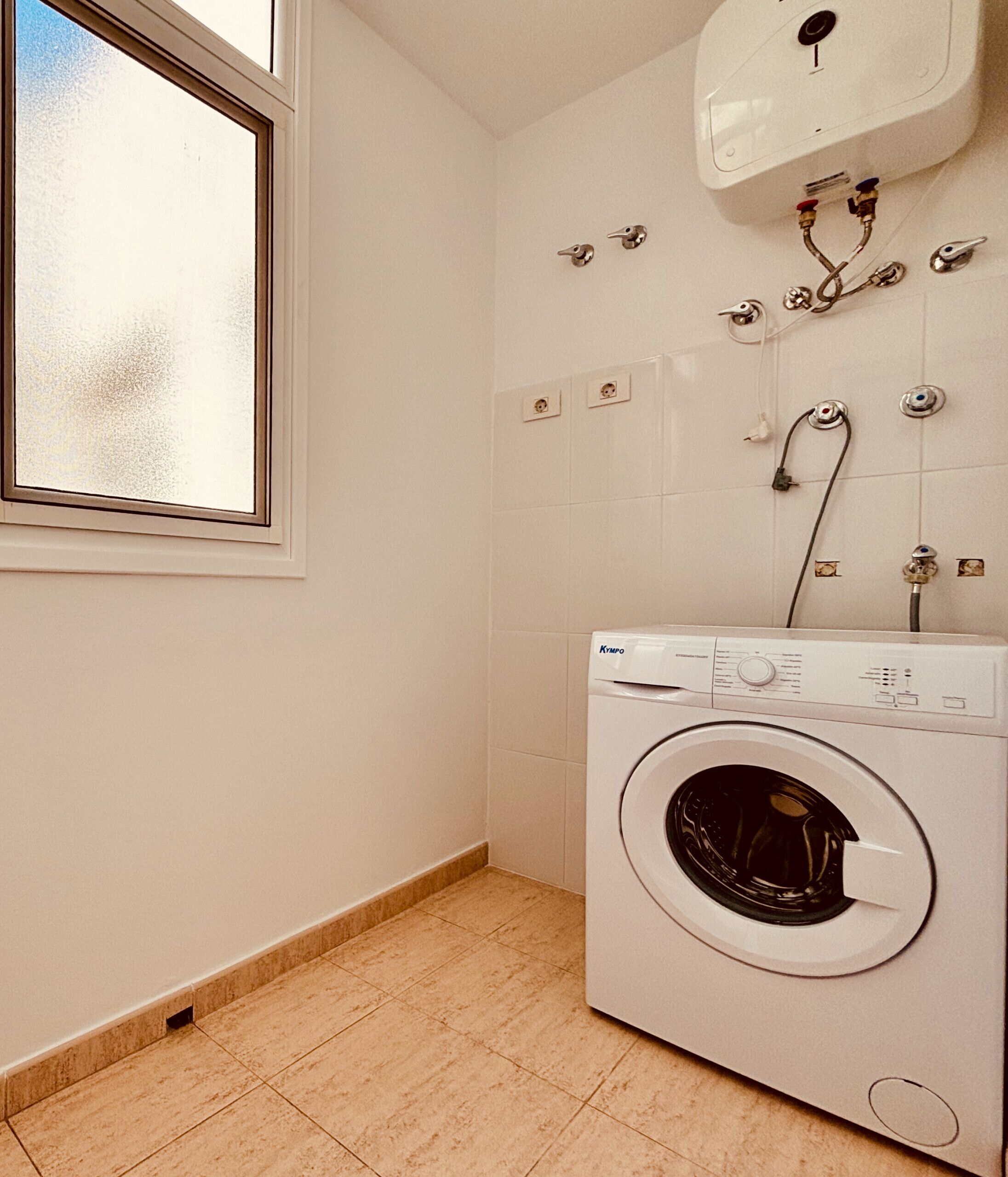 A laundry room with a front-loading washing machine, a window, and a wall-mounted water heater.