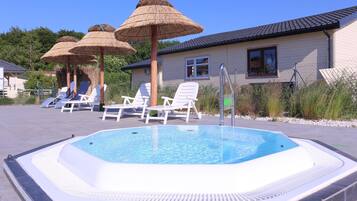 A swimming pool with lounge chairs and umbrellas, surrounded by a building with a tiled roof.