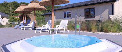 A swimming pool with lounge chairs and umbrellas, surrounded by a building with a tiled roof.