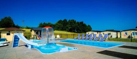 A swimming pool with a water slide, lounge chairs, and a small building in the background.