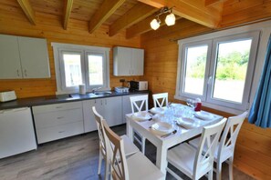 Una cabaña de madera con cocina, comedor y ventanas amplias.