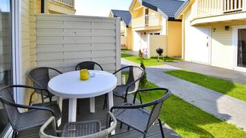 A patio with a round table and four chairs, a small yellow container, and a grill.