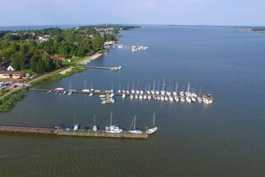 An aerial view of a marina with numerous boats docked, a bridge connecting to a land area with buildings, and a clear view of the surrounding landscape. - Holiday Cottage Near the Lake, Osieki (gmina Sianów)