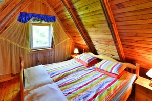 A cozy attic bedroom with a sloped ceiling, a window with a blue curtain, and a bed with striped bedding. - Holiday Cottage Near the Lake, Osieki (gmina Sianów)