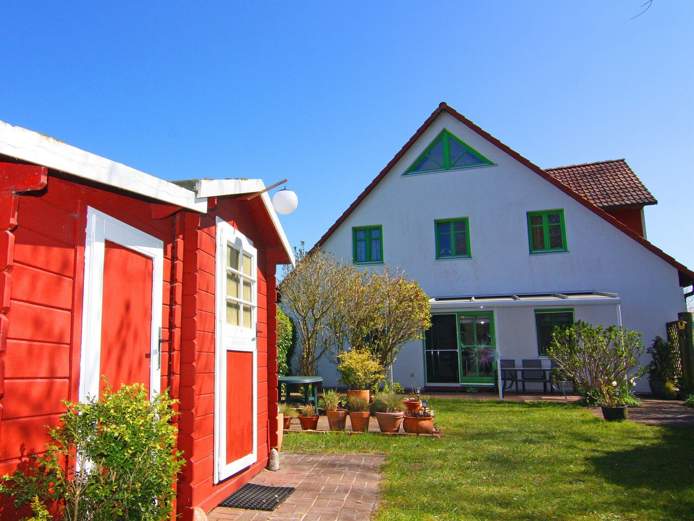 A two-story house with a red exterior and a white upper section, featuring a green window trim and a tiled roof.