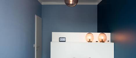 A bedroom with a bed, a nightstand, a wall clock, and a hanging light fixture.