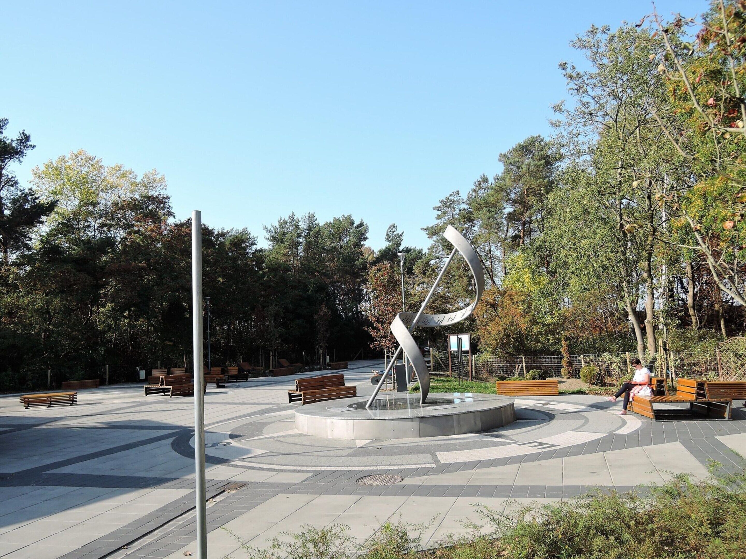 A public park with a central sculpture, benches, and trees.