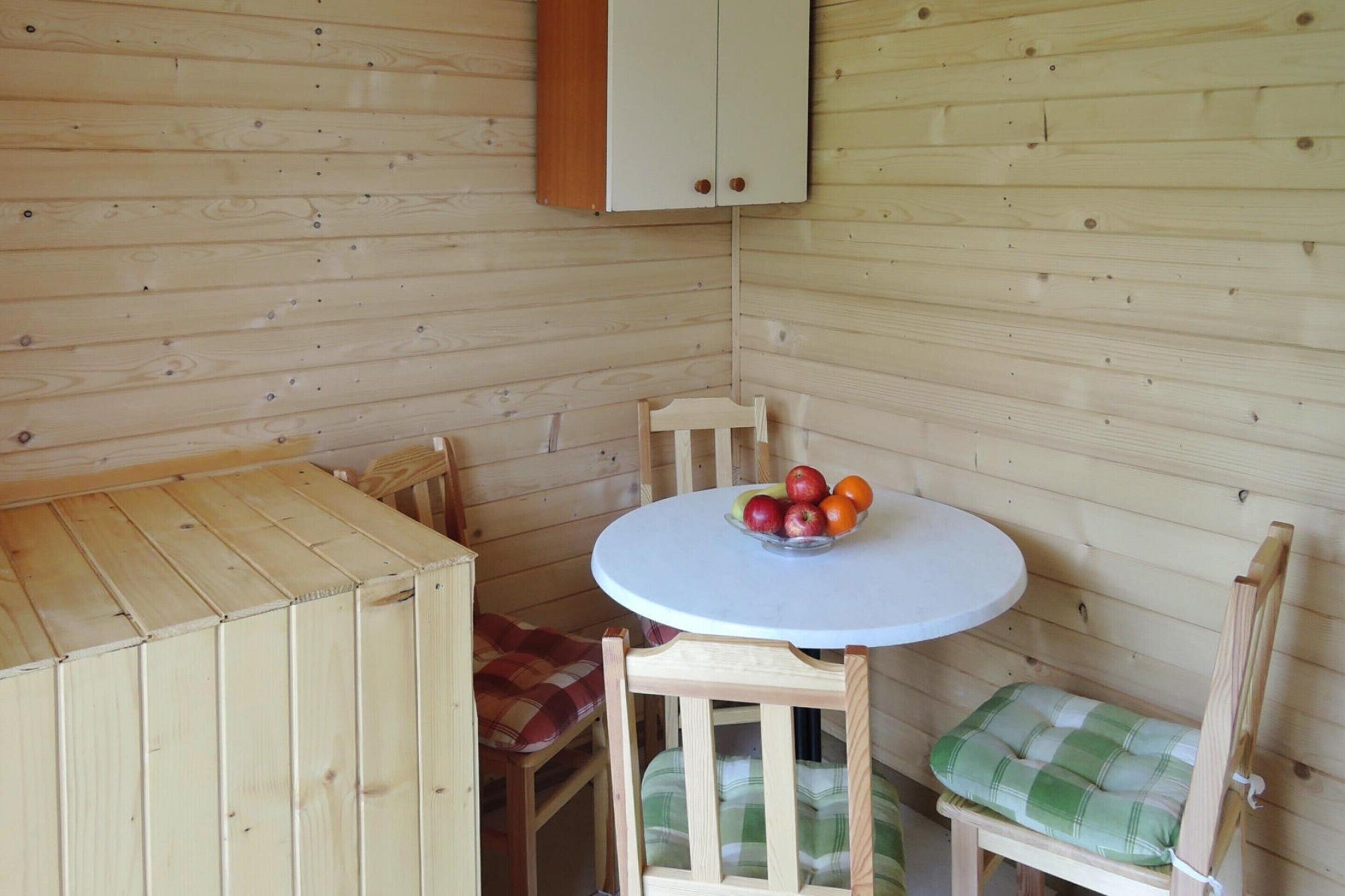 A wooden cabin interior with a round table, two chairs, and a cabinet.
