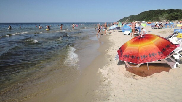 Ein Strand mit badenden Menschen und Spaziergängern, Sonnenschirmen und Liegestühlen.