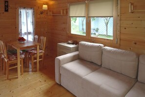 A wooden cabin interior with a dining table, chairs, a sofa, and a window with a view of the outdoors. - Holiday Home Near Baltic Sea and Nature Reserve (Kamien Pomorski)