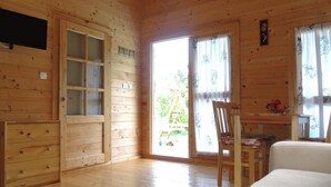 Eine Holzhütte mit Holztür, einem Fernseher, einem Esstisch mit Stühlen und einem Fenster mit Vorhängen.