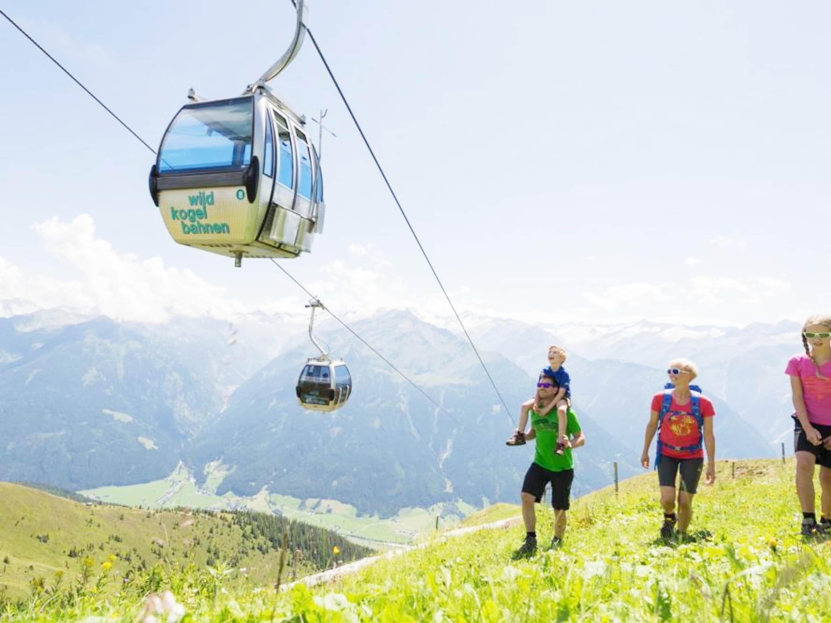 Une télécabine portant l’inscription « WILD KOGELBAHNEN », un paysage montagneux et des personnes qui se promènent.