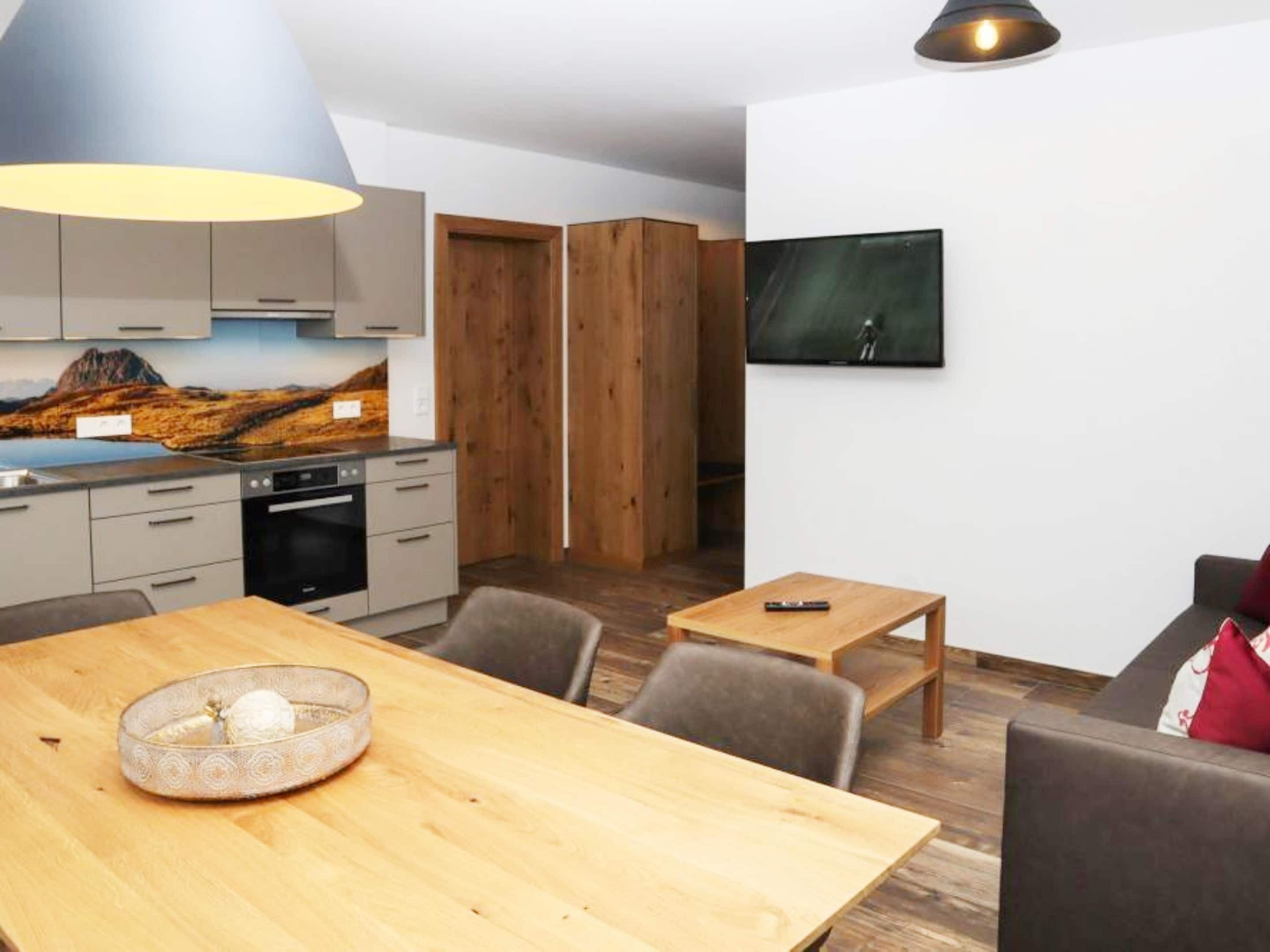 Een moderne keuken met grijze kastjes, een houten eettafel en een schilderij aan de muur.