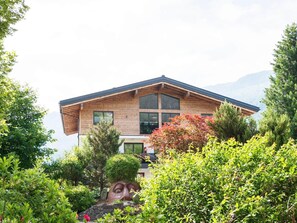 A modern two-story house with a sloped roof, large windows, and surrounded by lush greenery. - Apartment in Bramberg Near Cable Car (Bramberg am Wildkogel)