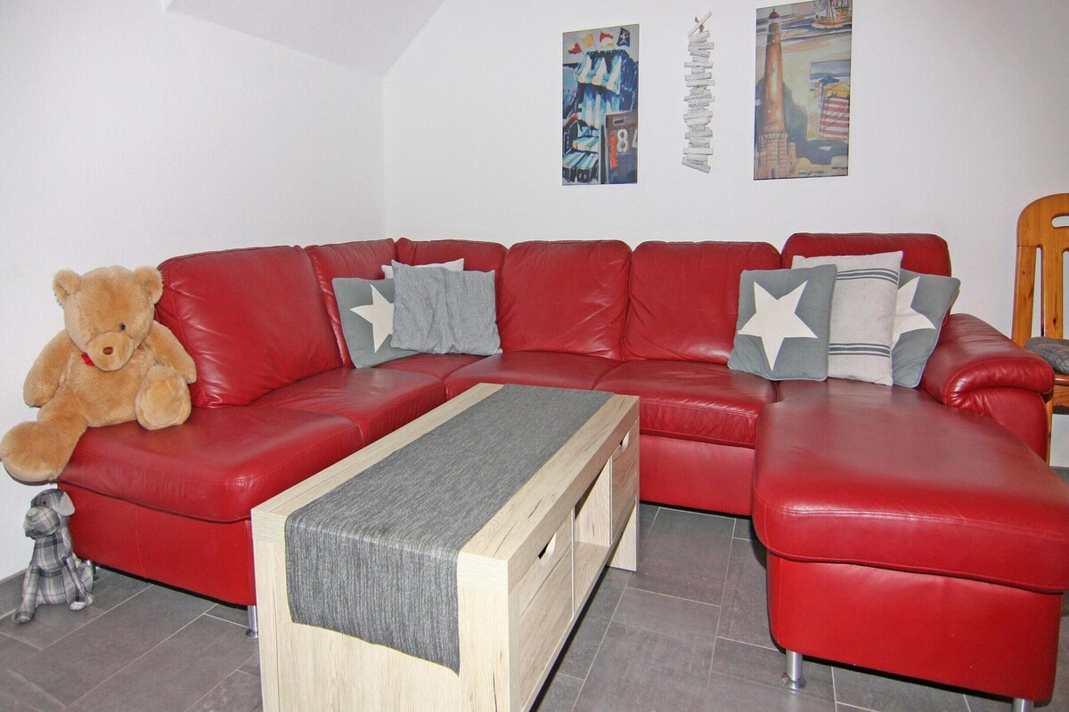 A red leather sectional sofa with a wooden coffee table, a teddy bear, and star-patterned pillows.