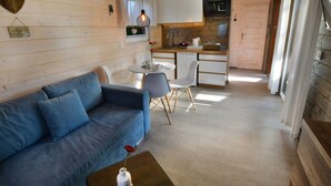 Un intérieur de chalet chaleureux avec un canapé, une table à manger, des chaises et un coin cuisine.