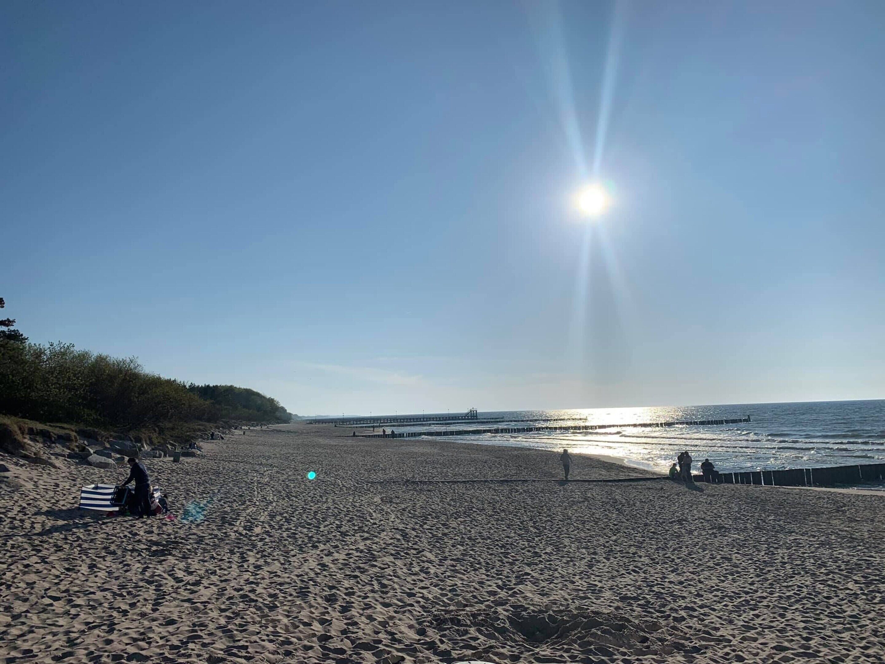 Ranta, josta ulottuu laituri veden päälle, kirkas taivas ja kirkkaasti paistava aurinko.