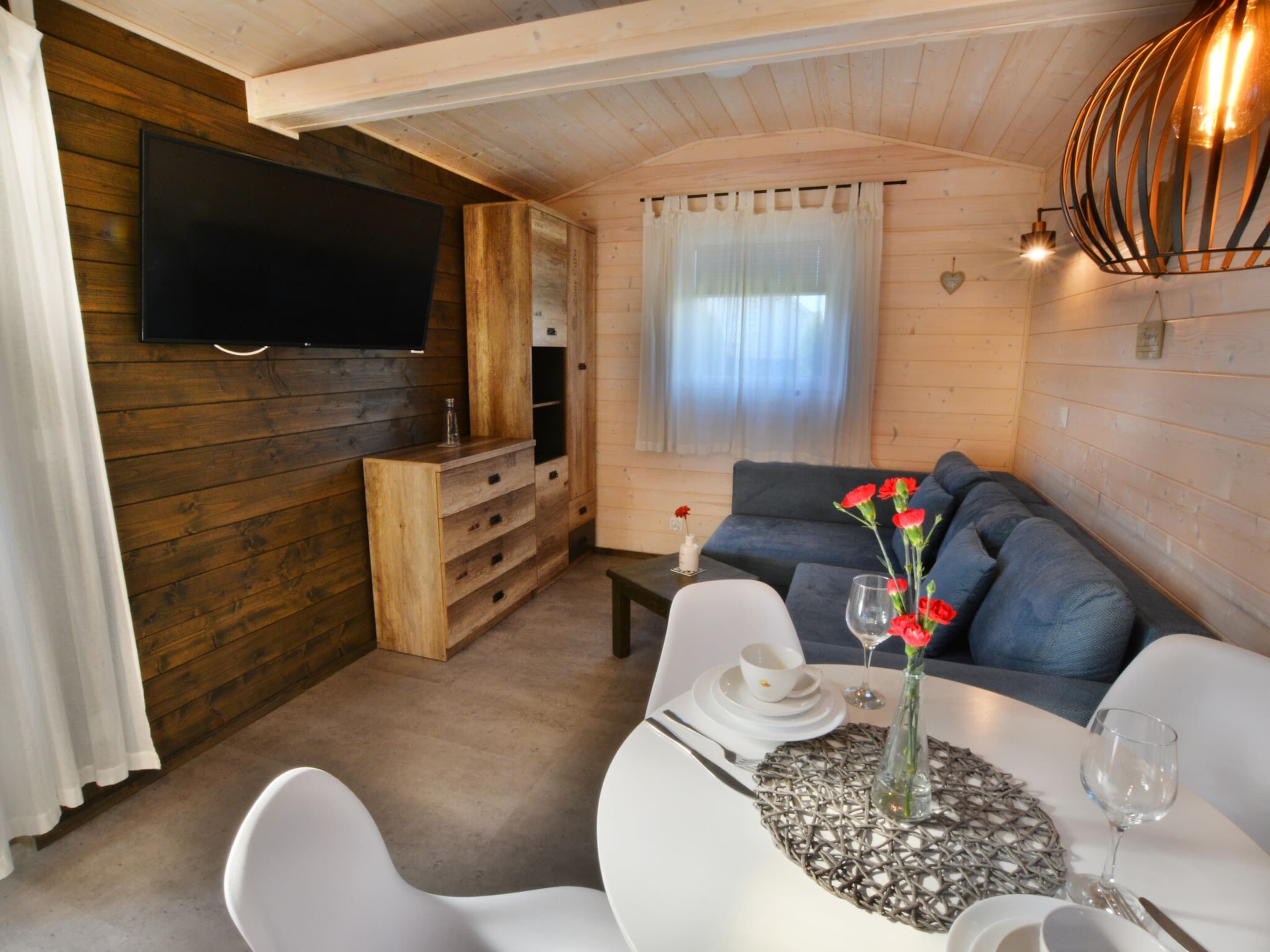 Una sala de estar acogedora con un televisor de pantalla plana, armarios de madera, un sofá y un comedor con una mesa dispuesta para dos.