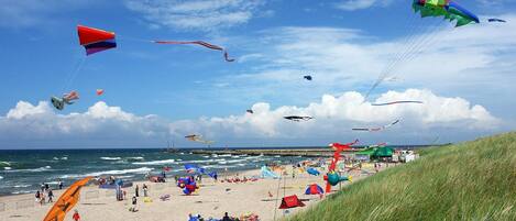 A beach with tents and people, and kites flying in the sky.