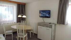 A hotel room with a dining table, chairs, a TV mounted on the wall, and a wardrobe. - Apartment in Ischgl at the ski bus Stop (Ischgl)