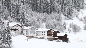 A snow-covered mountain lodge with multiple buildings, including a large white building with balconies and a smaller wooden structure. - Apartment in Ischgl at the ski bus Stop (Ischgl)