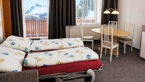 A hotel room with a bed, a dining table, chairs, a desk, and a window with curtains. - Apartment in Ischgl at the ski bus Stop (Ischgl)