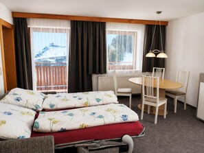 Una habitación de hotel con cama, una mesa de comedor, sillas, un escritorio y una ventana con cortinas.