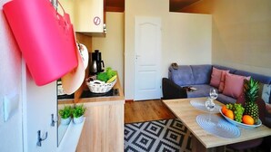 Ein gemütlicher Wohnraum mit Küchenzeile, einer Essecke mit Tisch und Stühlen, einer Couch und einem kleinen Couchtisch mit Obst und einem Glas.