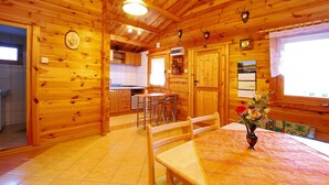 Ein Interieur einer Holzhütte mit Esstisch, Stühlen, einer Küchenzeile und einem Fenster mit Vorhängen.