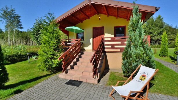 Ein zweistöckiges Gebäude mit einer Holztreppe, einem grünen Sonnenschirm und einem Liegestuhl mit der Aufschrift 'Bahama Leisure' auf der Terrasse.