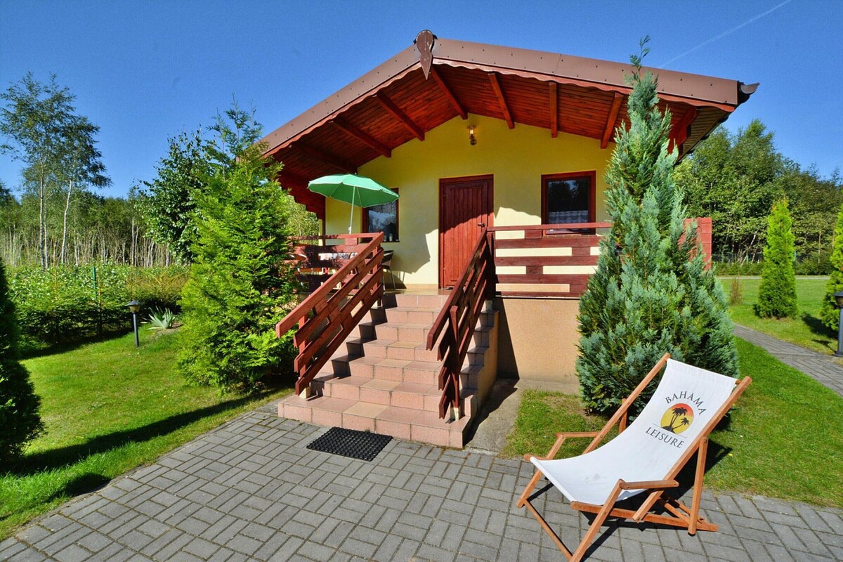 Un bâtiment à deux étages avec un escalier en bois, un parasol vert et une chaise de plage portant l’inscription « Bahama Leisure » sur la terrasse.