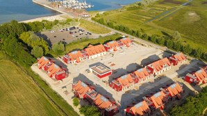 Vista aérea de una zona costera con un puerto deportivo, un estacionamiento y un conjunto de edificios con techos rojos.